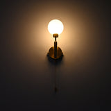 Illuminated raw brass globe wall sconce with round frosted globe, vertical stem, circular backplate and pull chain