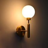 Illuminated raw brass globe wall sconce with round opal globe, vertical stem, circular backplate, and pull chain.