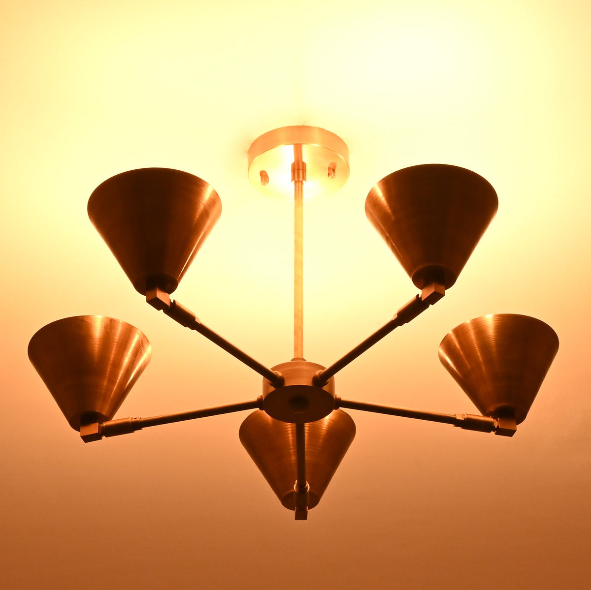 Five-light brass cone chandelier viewed from below, showcasing soft ambient illumination and industrial elegance.