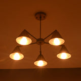 Five-light brass cone chandelier illuminated at night, casting warm ambient light in a modern interior setting.