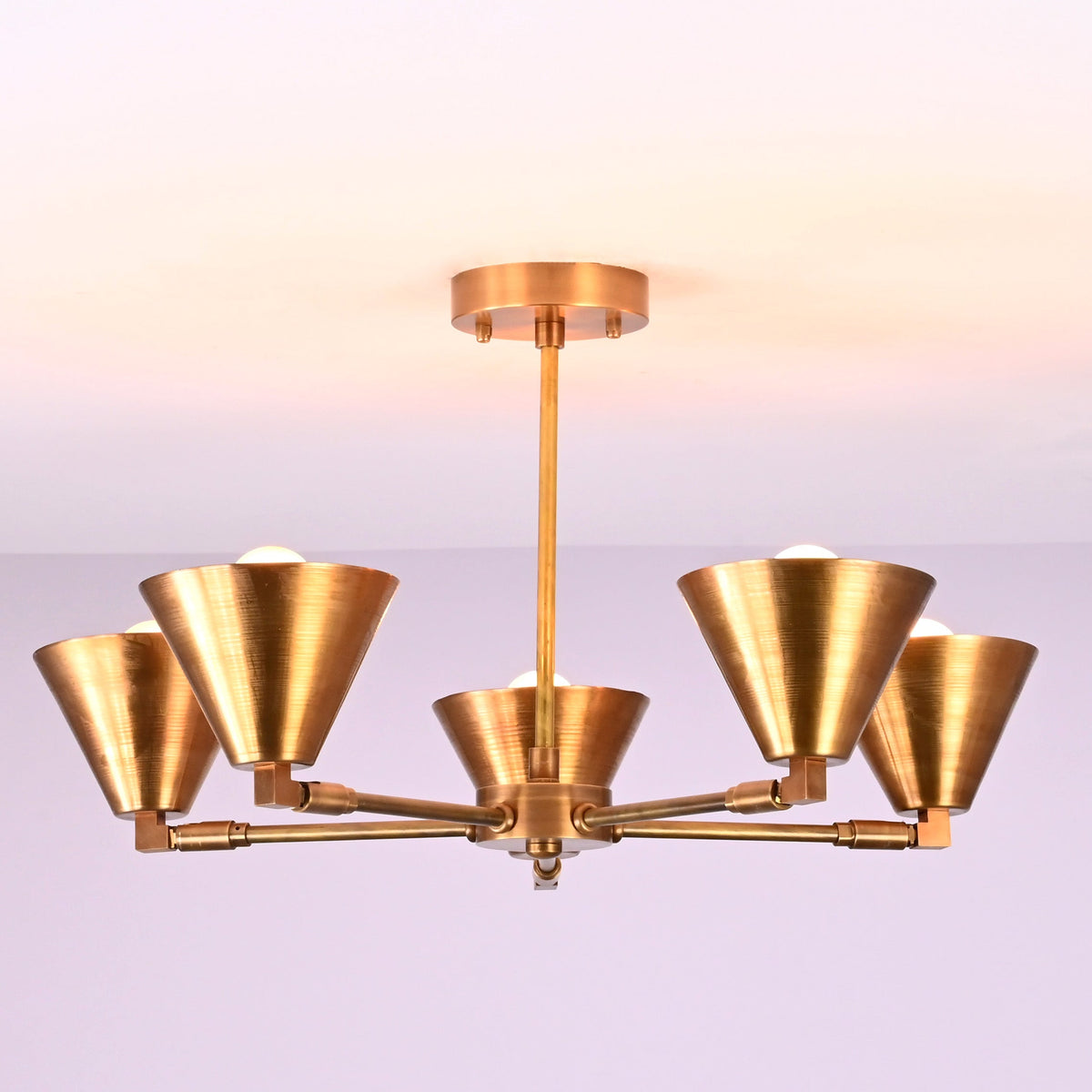 Ceiling-mounted five-light brushed brass chandelier with balanced arms and cone-shaped shades.