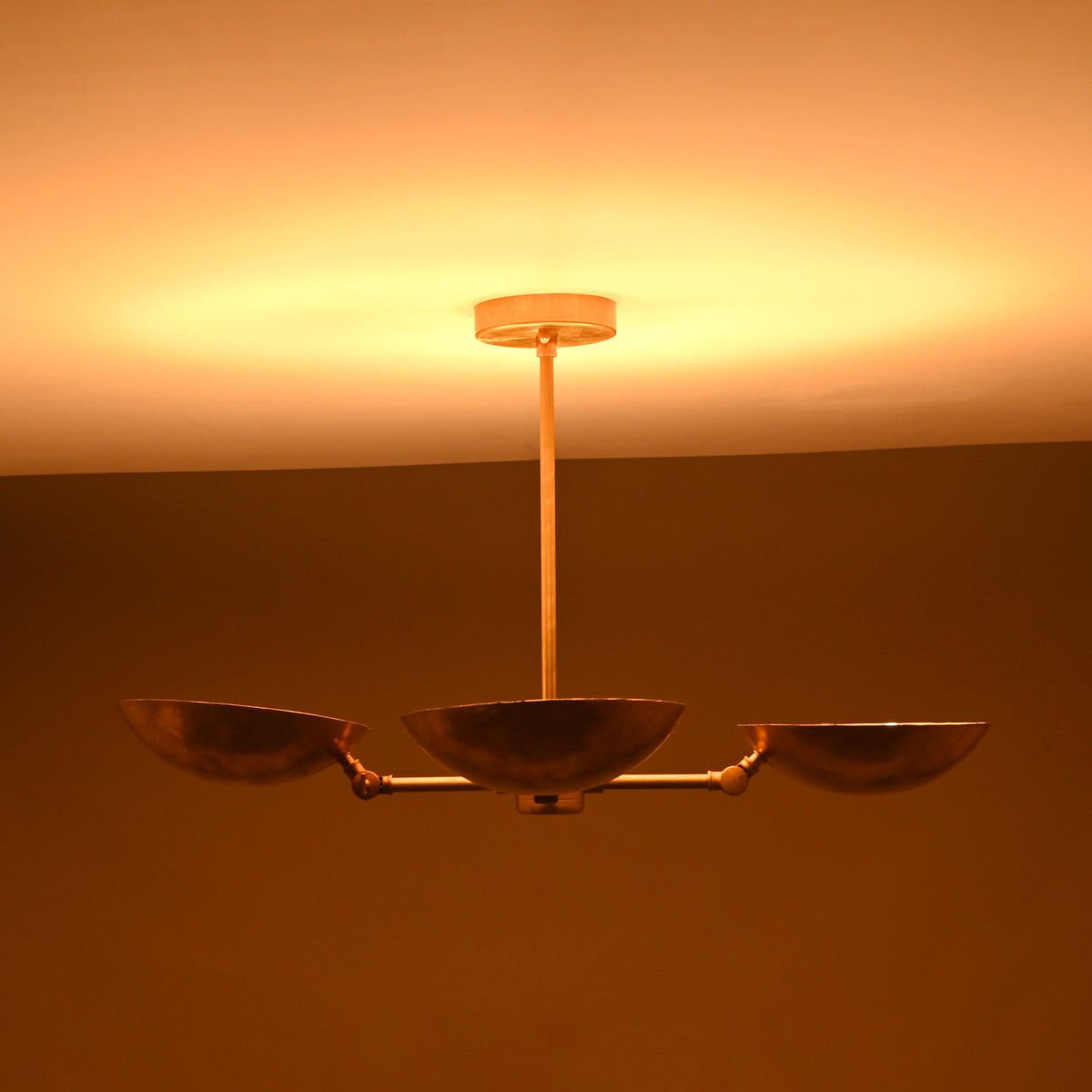 Four-bowl brass chandelier photographed in low lighting, showing deep golden glow and atmospheric ceiling illumination.