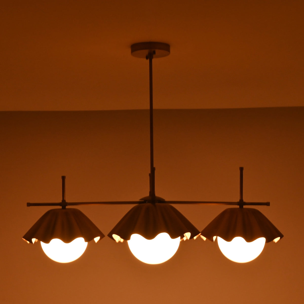 Bottom view of four-light brass chandelier showcasing warm indirect lighting and scalloped shade edges.