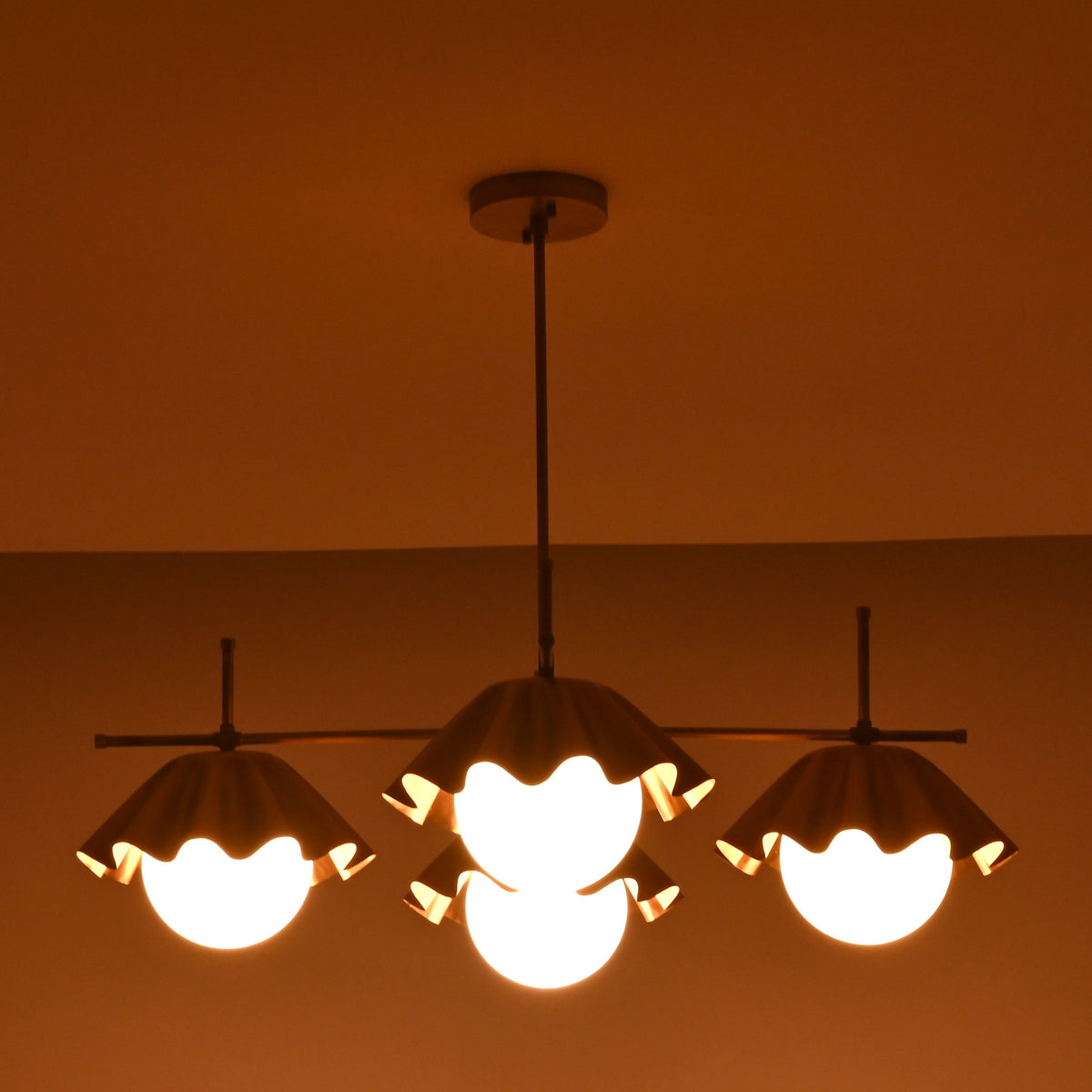 Wide linear view of four-light brass chandelier producing warm, diffused ambient illumination.