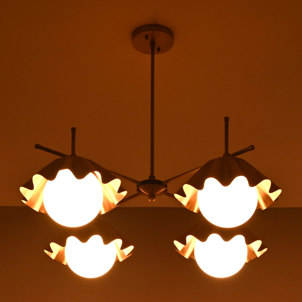 Top view of four-light brass chandelier glowing warmly with sculpted bowl-shaped shades.