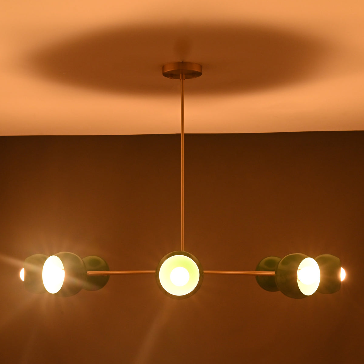 Close up of green bowl shaped metal shade on brass sputnik chandelier showing smooth finish and warm bulb reflection