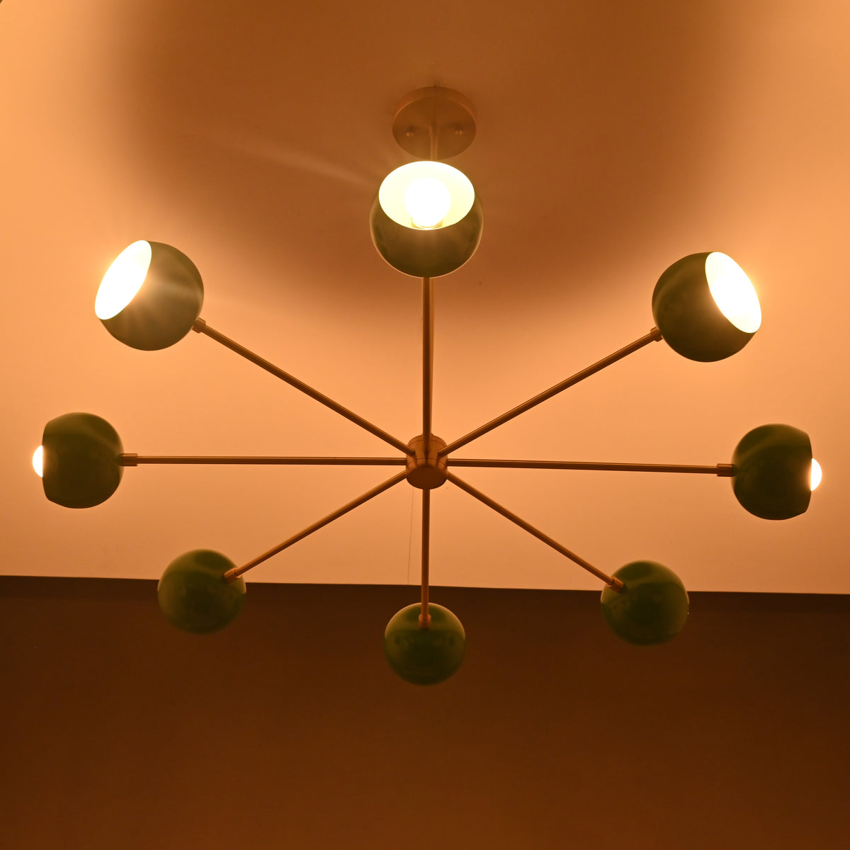 Green bowl sputnik chandelier casting warm indirect light across ceiling with soft modern ambiance