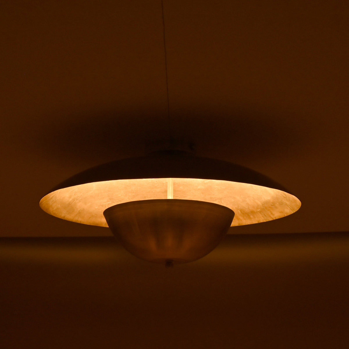 Handcrafted brass disc light with soft inner glow highlighting its smooth circular form in a dimly lit room