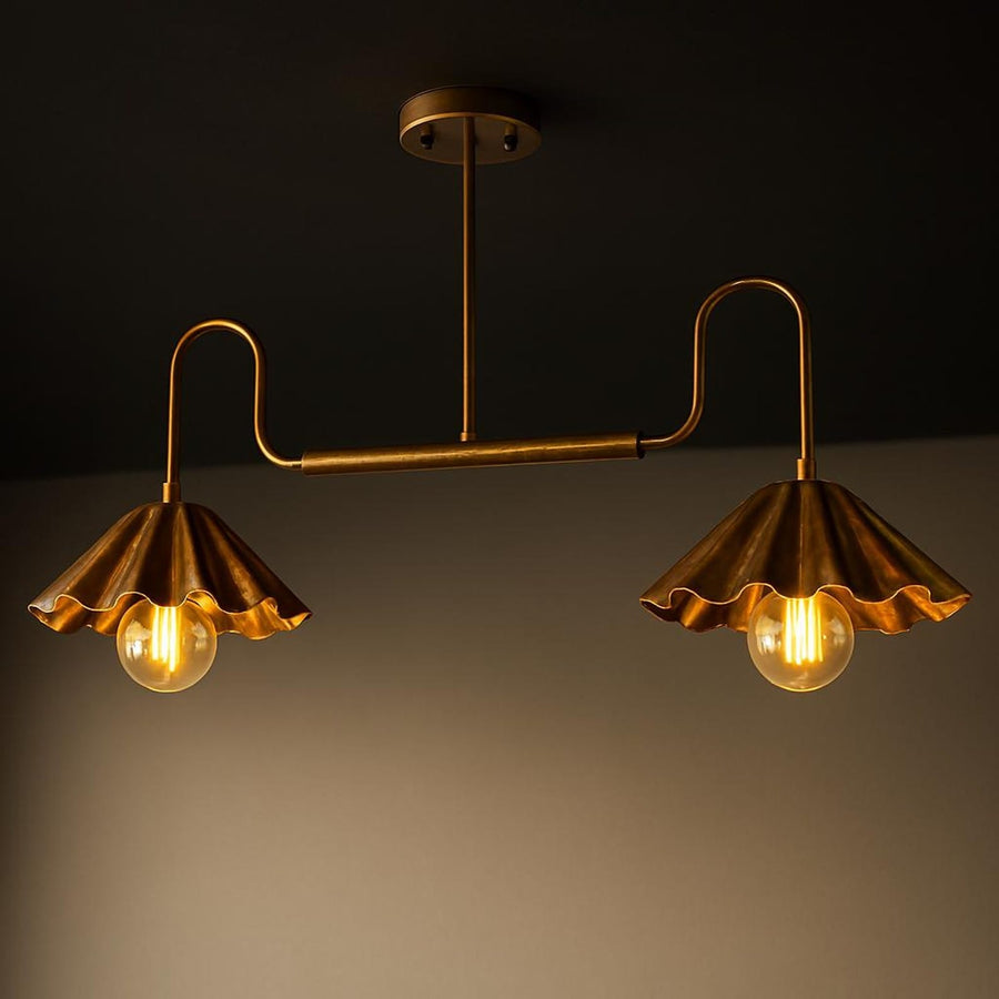 Modern brushed brass 2-light disc chandelier with scalloped bowl shades installed above a bedroom bed, providing warm ambient lighting