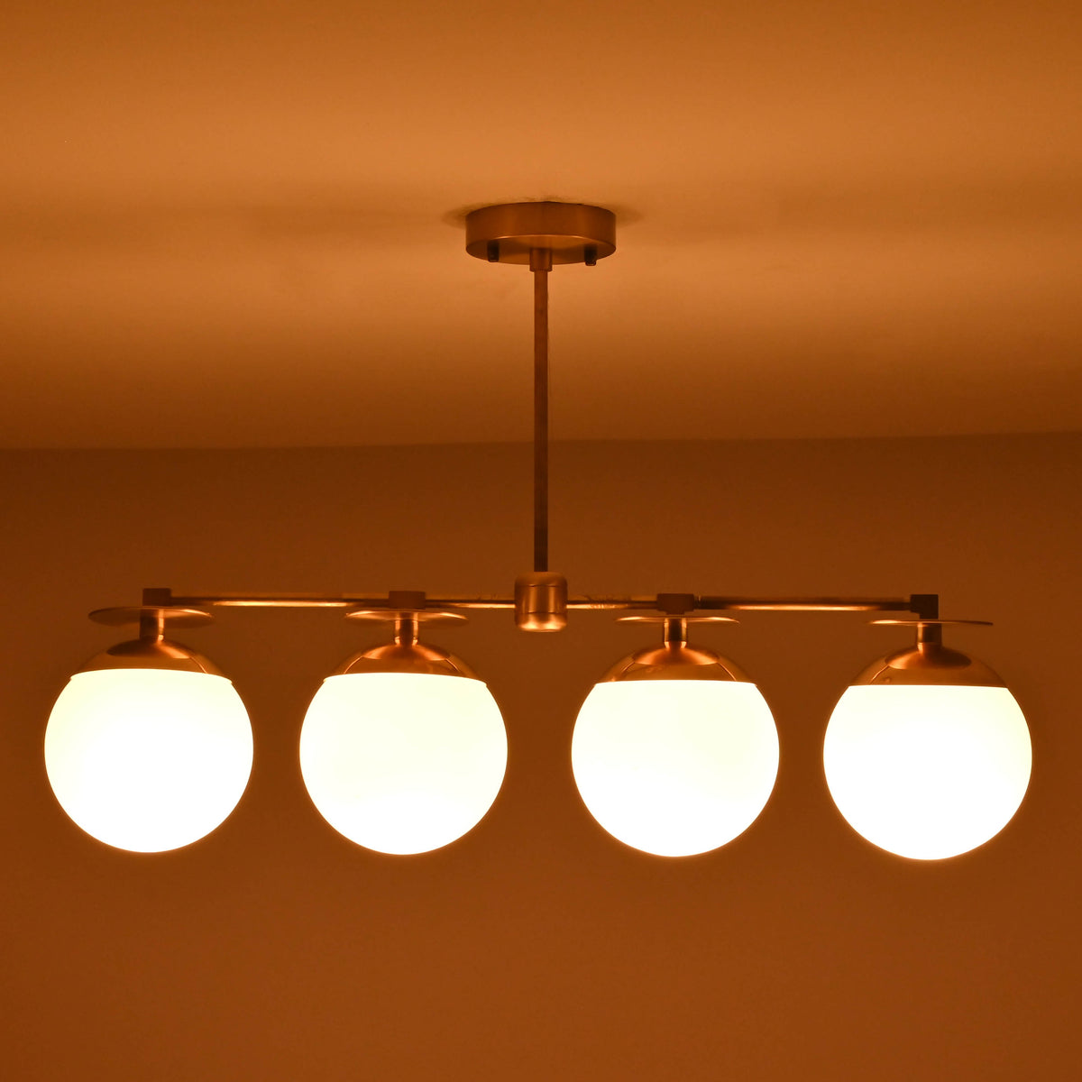 Industrial style brass linear chandelier with opal glass globes shown in warm low-light ambiance.