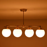 Industrial style brass linear chandelier with opal glass globes shown in warm low-light ambiance.