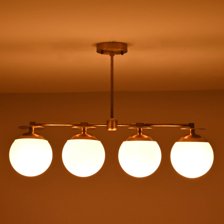 Front view of 4 linear brass chandelier with opal glass globe shades, showcasing minimalist industrial design and warm ambient lighting.