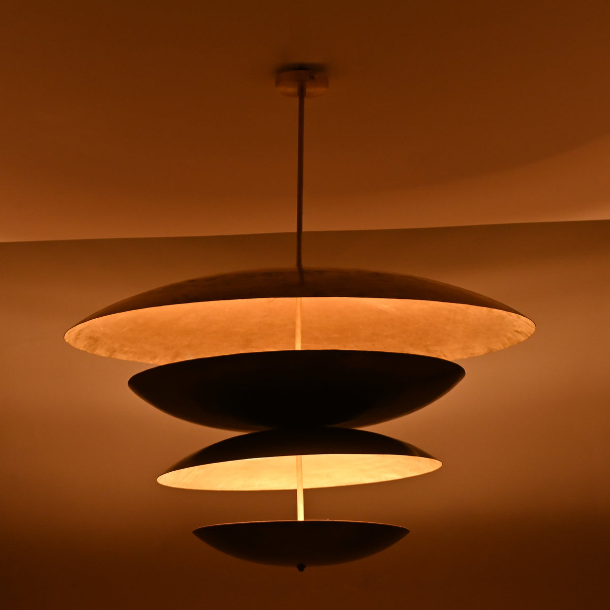 Warm ambient lighting effect from sculptural layered disc chandelier showing soft golden illumination through brass interiors.
