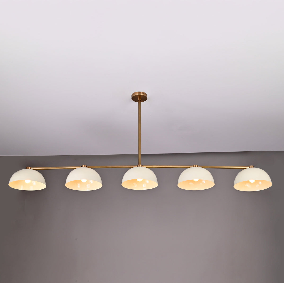Full front view of 5-light linear brass chandelier with enamel dome shades and downrod ceiling mount in neutral interior