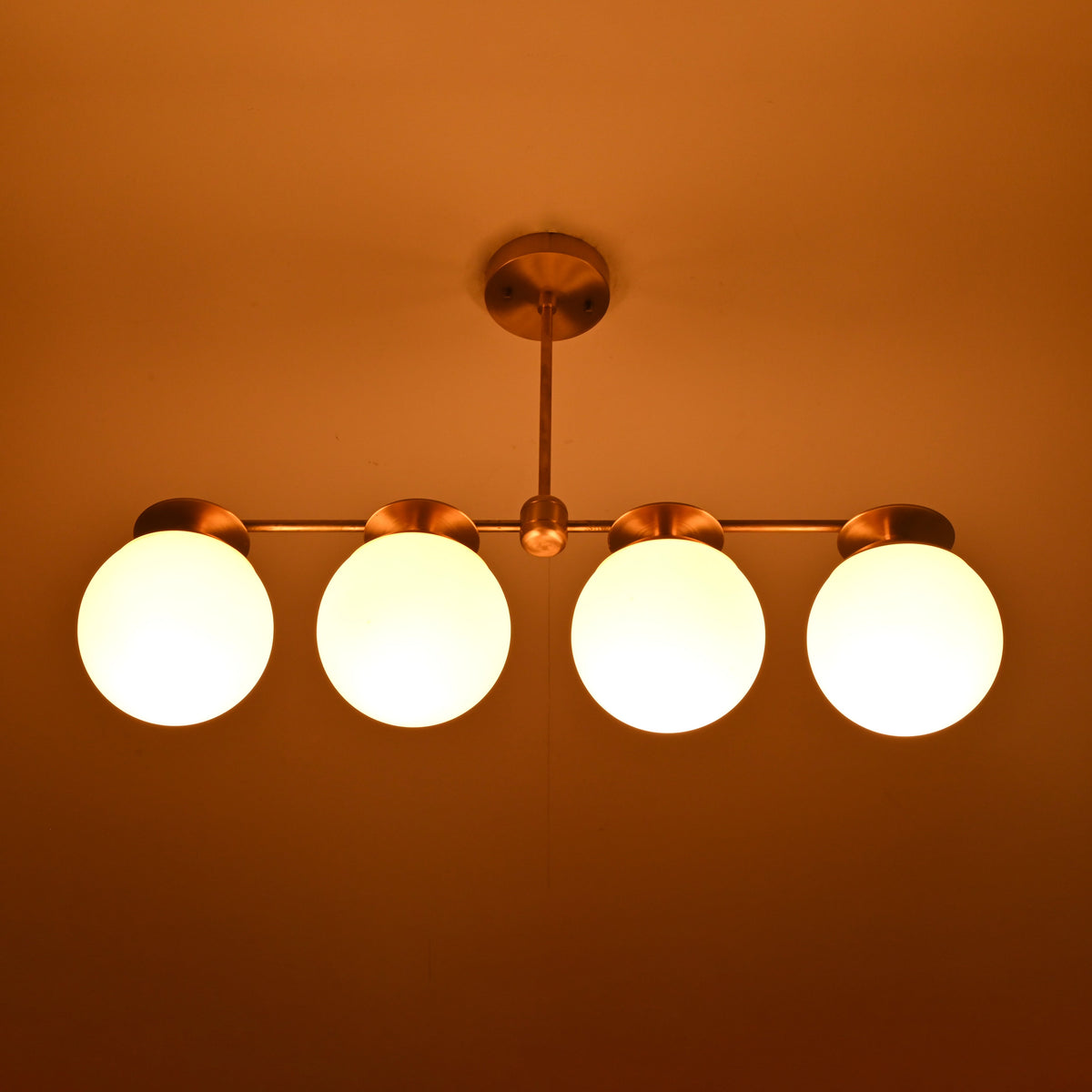 Night view of handcrafted brass linear chandelier with opal glass globes emitting warm, diffused lighting.