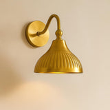 Luxury brushed brass wall lamp with curved arm and fluted shade mounted on wooden panel wall.