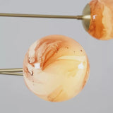 Close-up of handcrafted marble glass globe shade showing natural swirled patterns and warm glow on a solid brass chandelier.