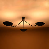 Three-arm ceiling fixture in matte black brass finish spreading warm diffused light across the ceiling