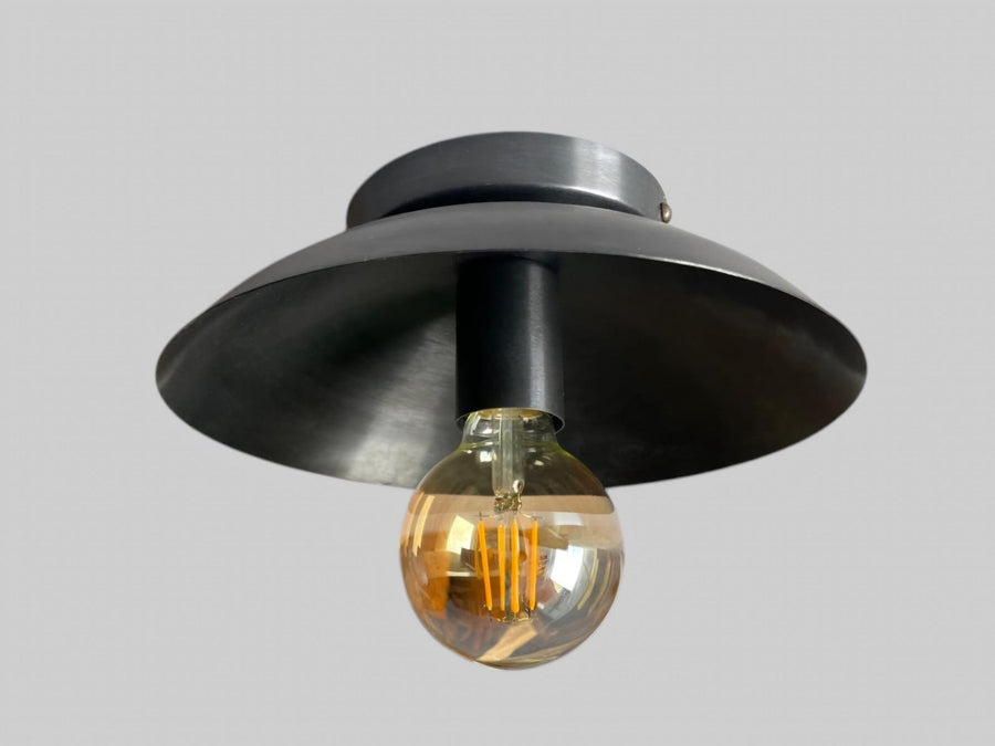 Close view of handcrafted blackened brass flush mount ceiling light featuring dome shade and Edison bulb by Brass Leaf Studio.