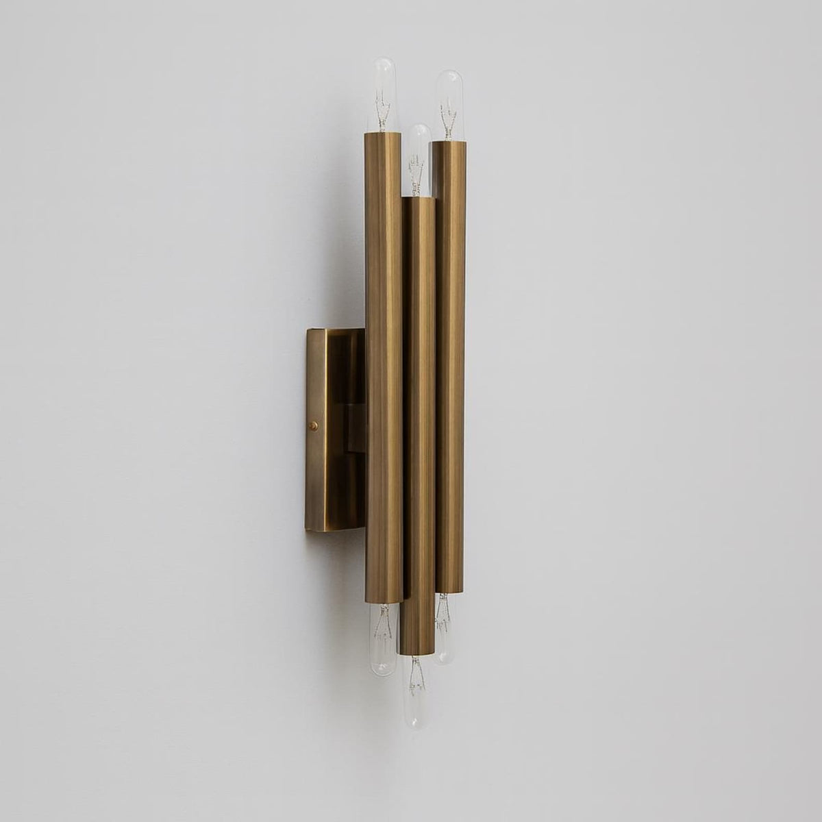 Mid century modern brass 6 light wall sconce featuring vertical cylindrical tubes and minimalist rectangular backplate