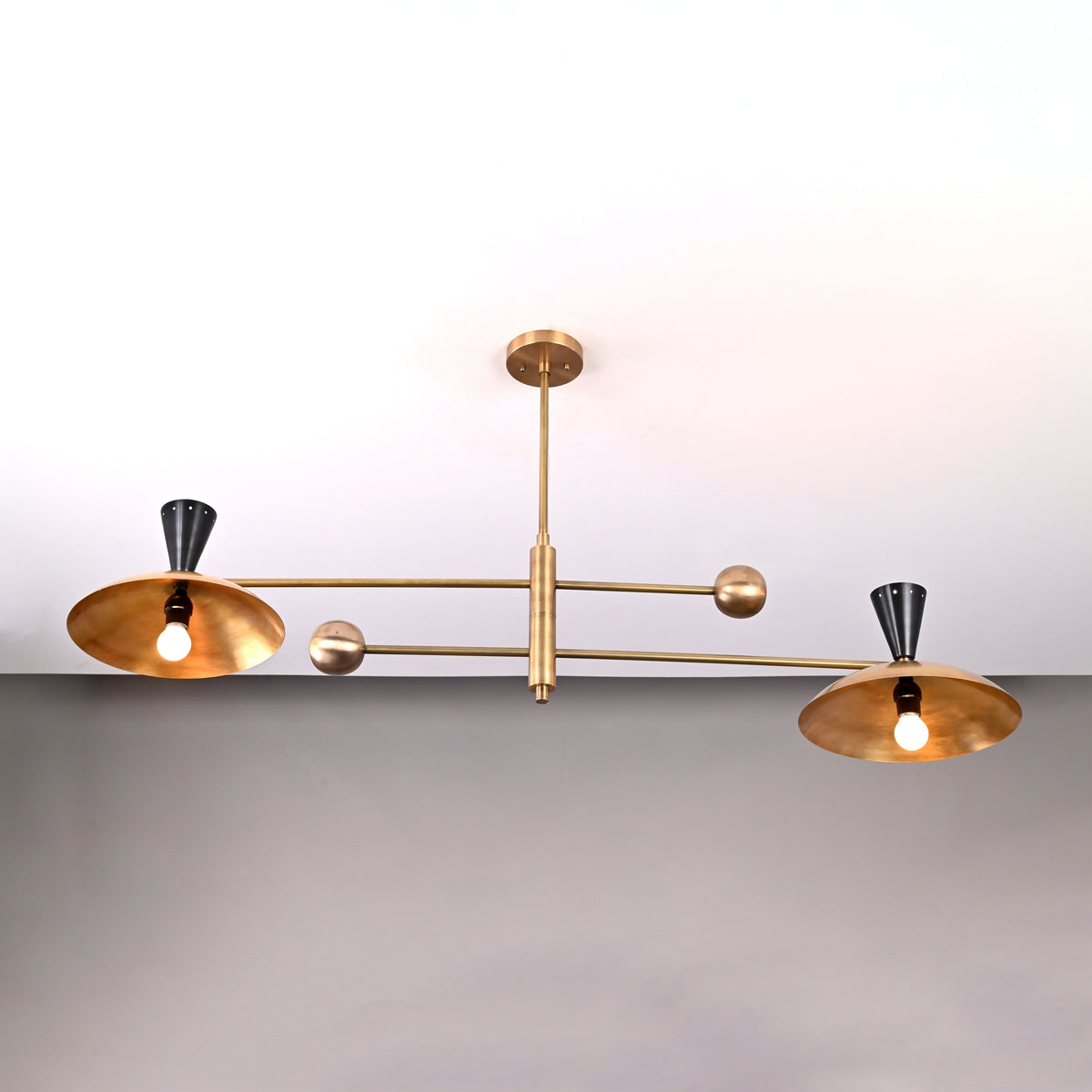 Side angle of mid-century inspired Diabolo chandelier featuring two wide brass shades and sculptural cone details.