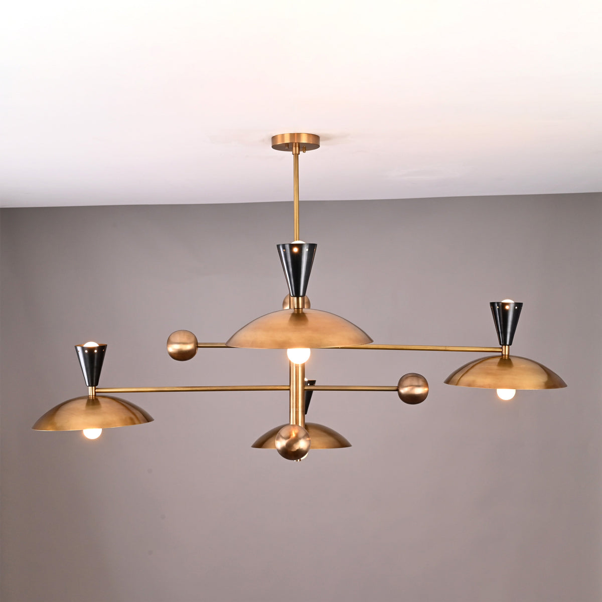 Side angle of mid-century modern Diabolo brass chandelier featuring eight bowl-shaped brass shades and black cone sockets.