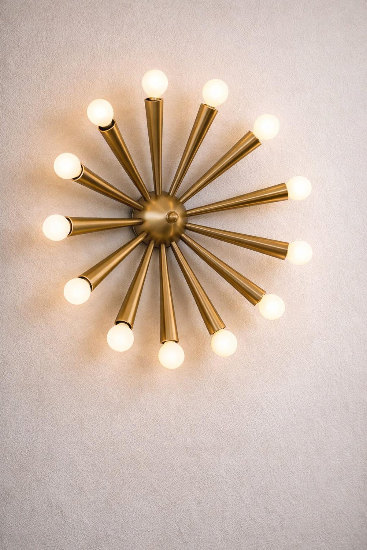 Close-up of a handcrafted mid-century brass starburst wall light with solid brass arms and glowing spherical bulbs.