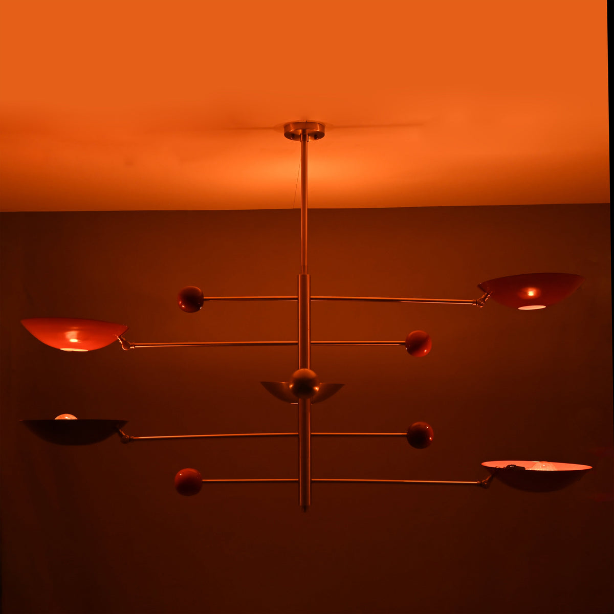 Mid-century modern mobile chandelier featuring brushed brass construction and red bowl shades arranged on balanced rods.