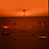 Mid-century modern mobile chandelier featuring brushed brass construction and red bowl shades arranged on balanced rods.
