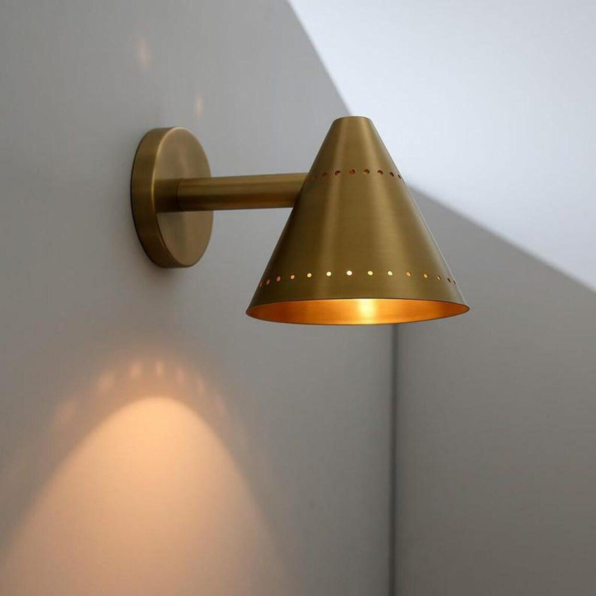 Handcrafted brass cone wall sconce mounted on a neutral wall, showcasing its clean minimalist form and brushed brass finish.