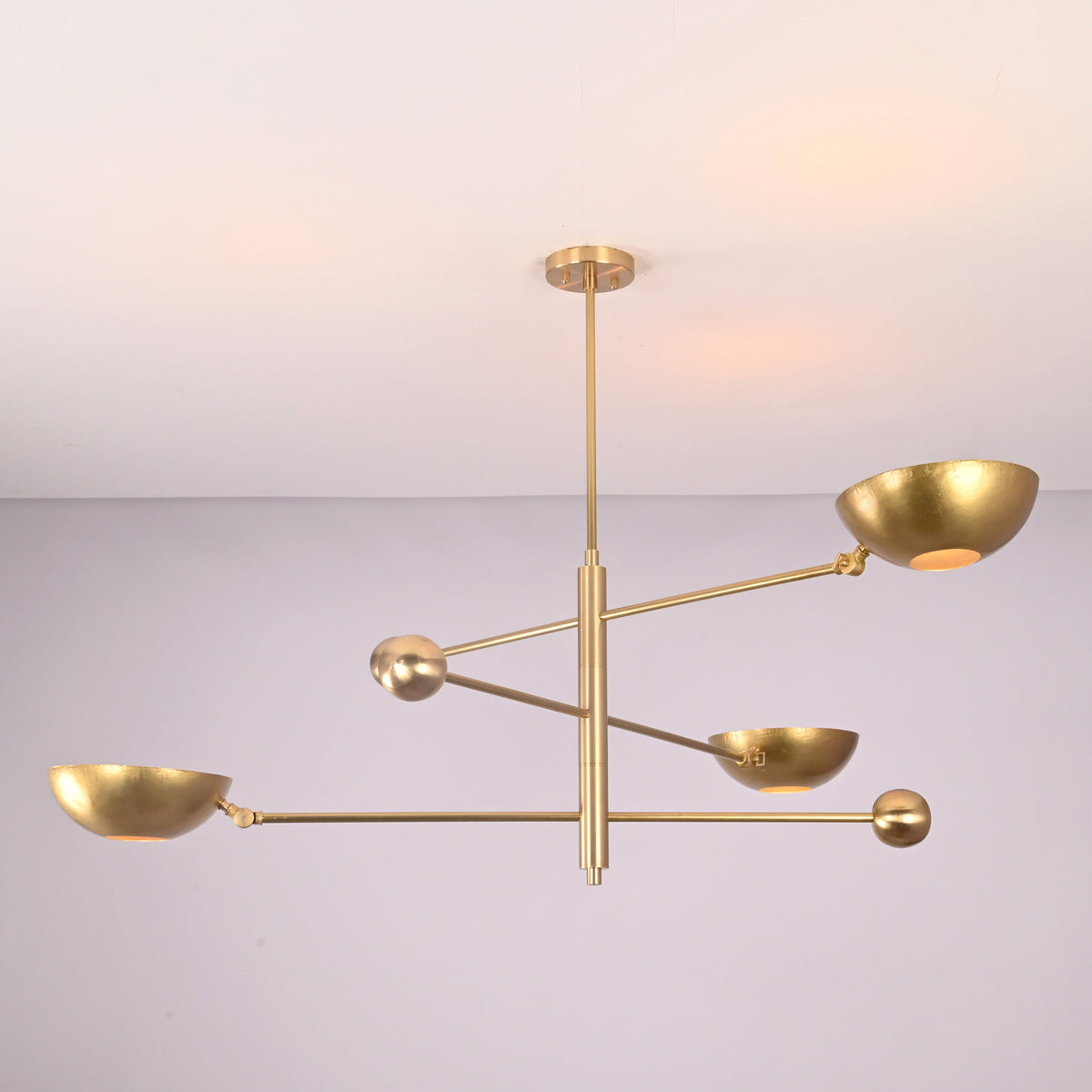 Angled view of minimalist brass disc chandelier showcasing sculptural arms and bowl shades