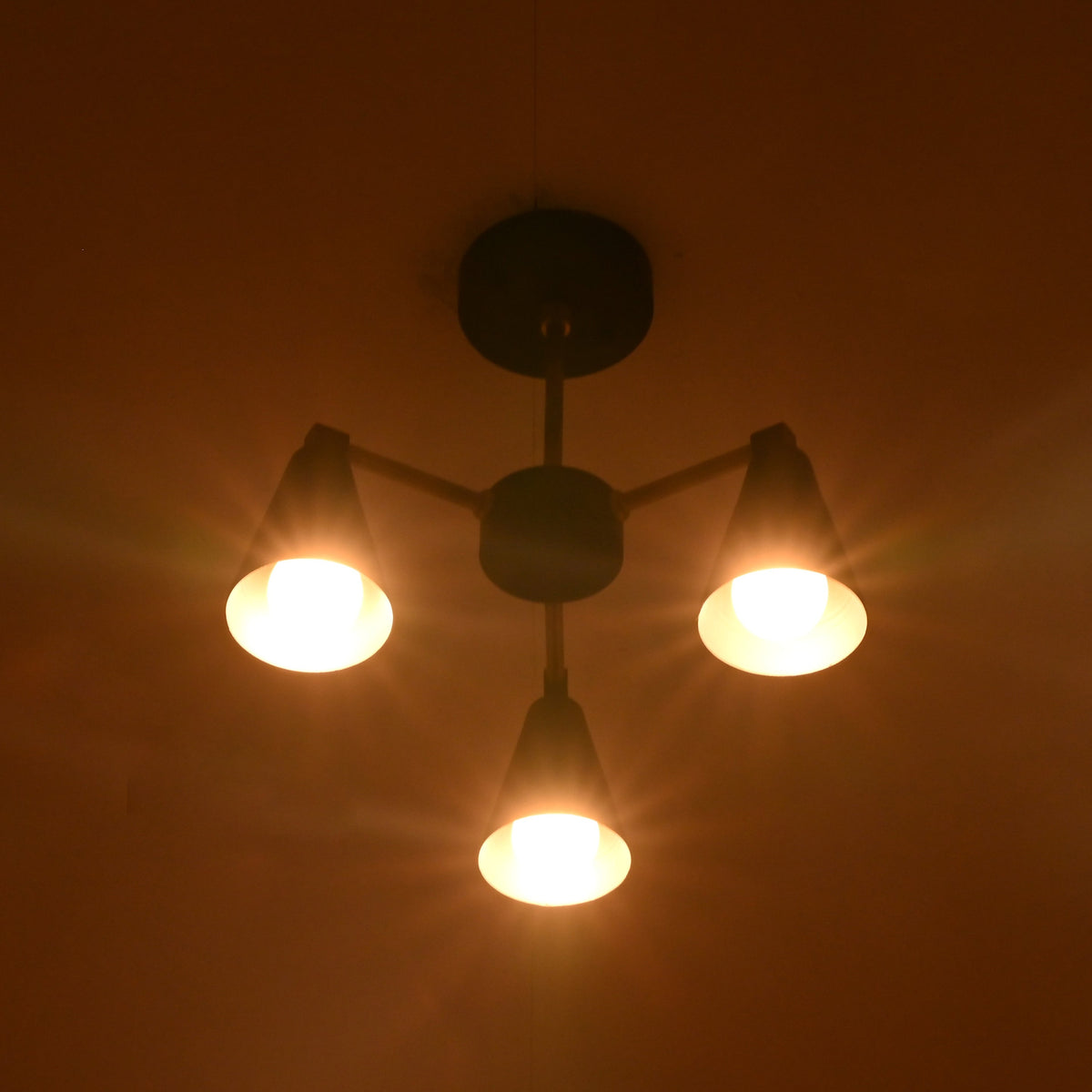 Bottom view of minimalist cone chandelier with three warm glowing lights