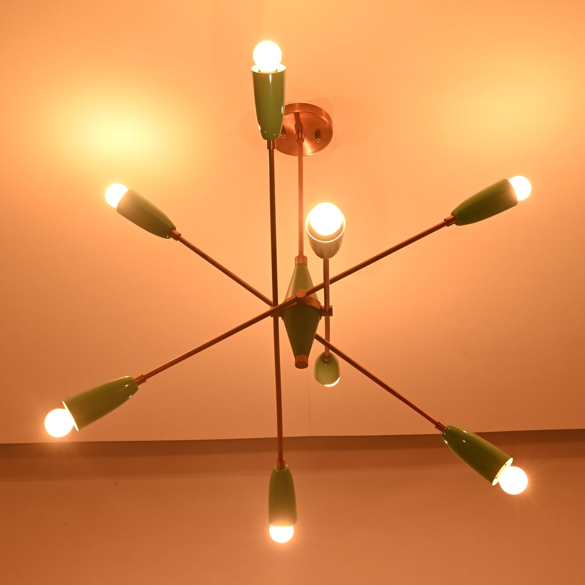 Angled dark room view of mint green 8 light brass chandelier with glowing bulbs and copper accents.