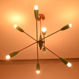 Angled dark room view of mint green 8 light brass chandelier with glowing bulbs and copper accents.