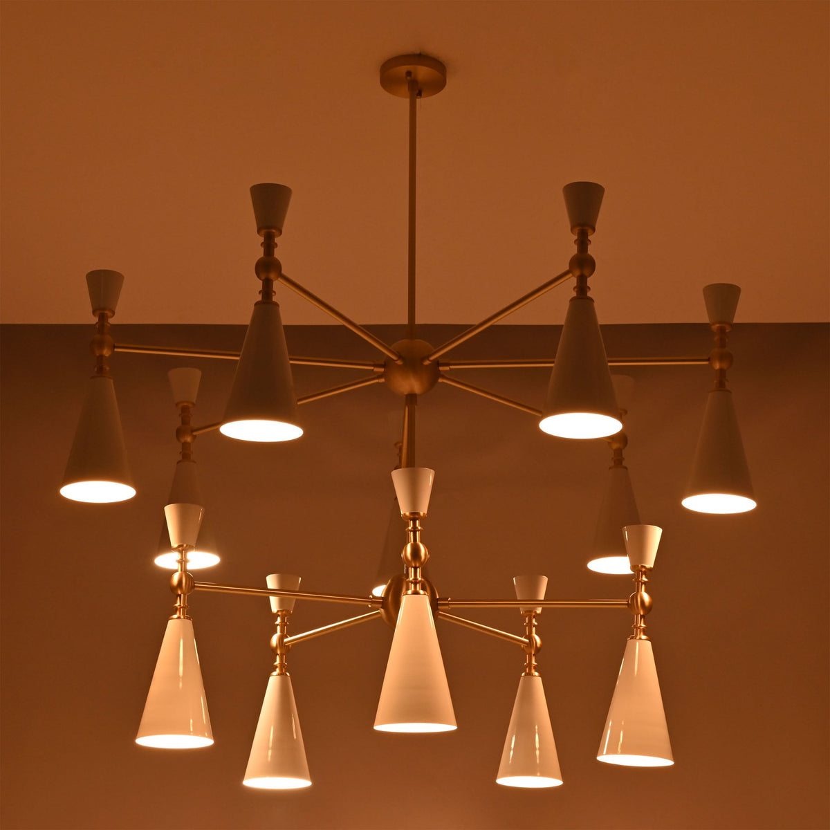 Modern 12-light cone chandelier shown on white background with brushed brass structure and white enamel painted shades