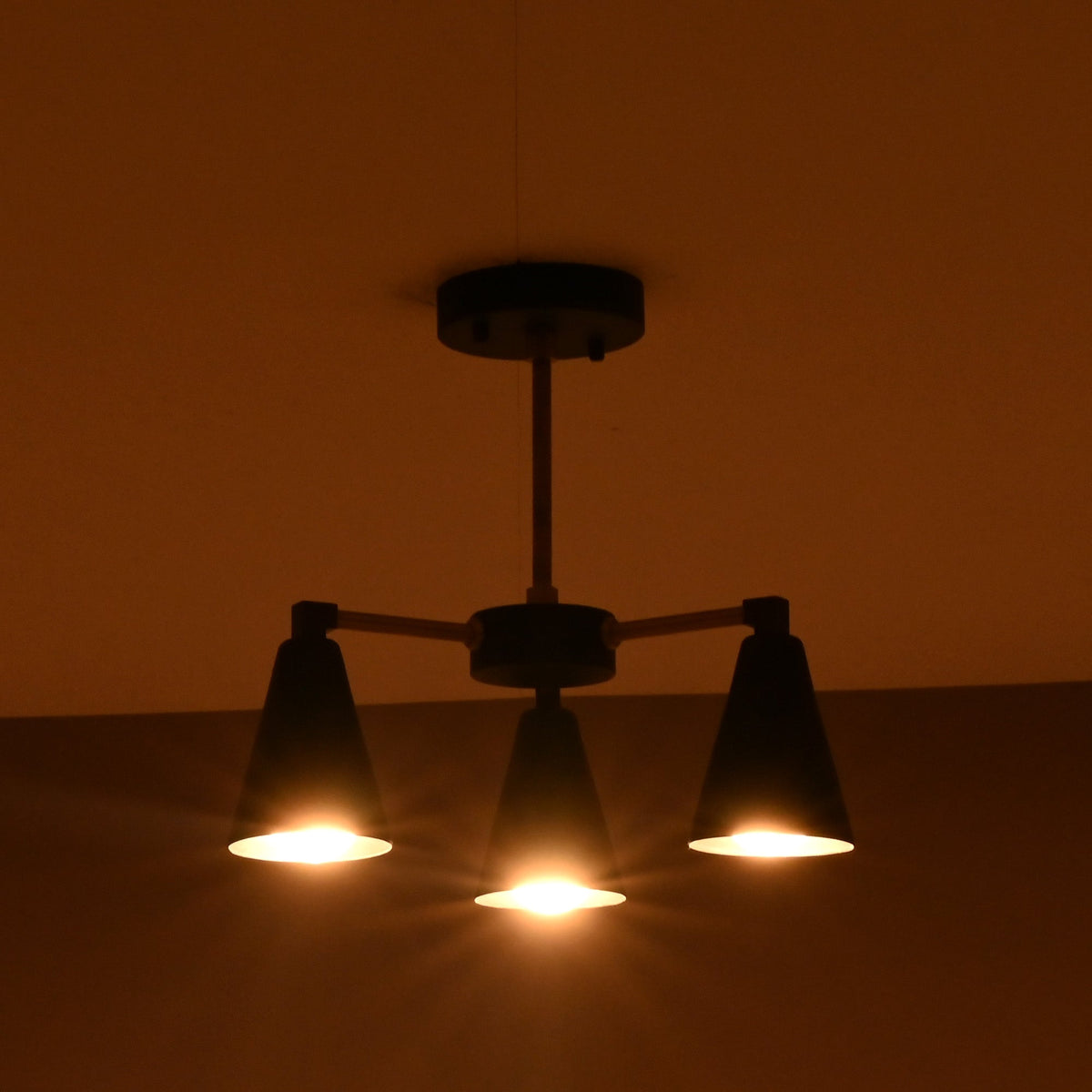 Modern three light cone chandelier fully illuminated showing warm focused light distribution