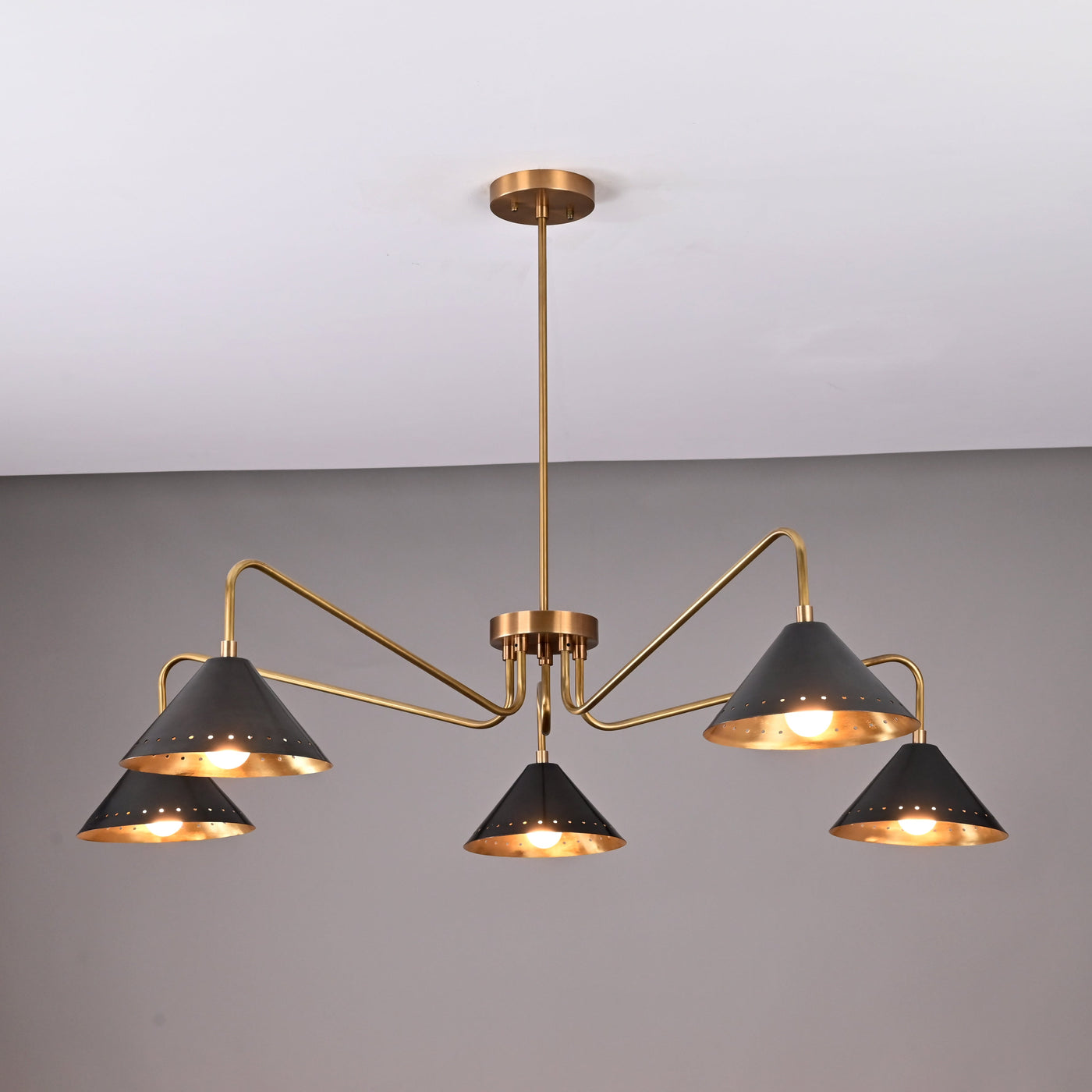 Front view of handcrafted 5-light brass chandelier featuring matte-black perforated cone shades and brushed brass arms.