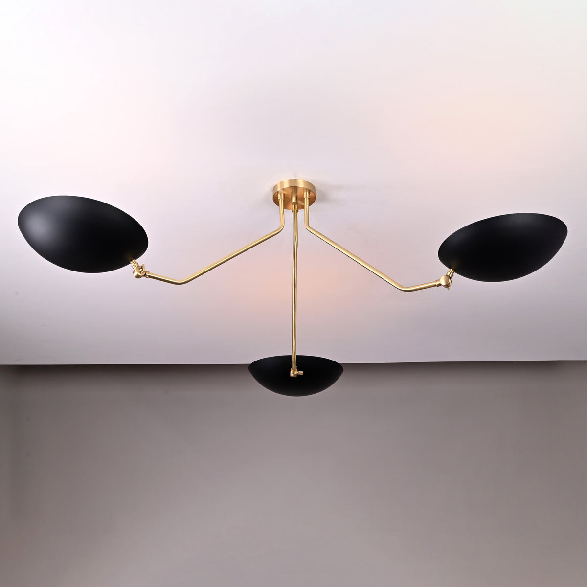 Modern sculptural chandelier with three black bowl shades and brass arms, designed for wide ceiling coverage.