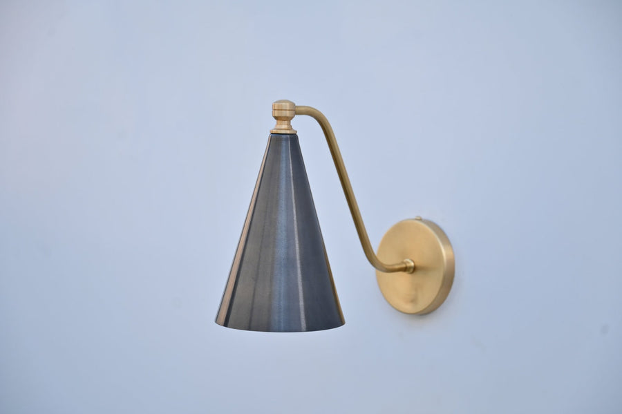 Blackened brass cone wall light casting a warm ambient glow, featuring brushed brass arm and round wall mount.