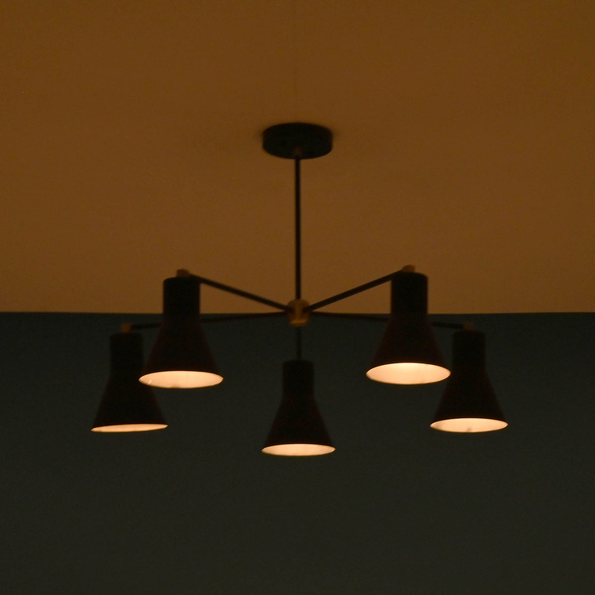 Atmospheric view of 5 cone brass chandelier casting warm industrial lighting in modern space