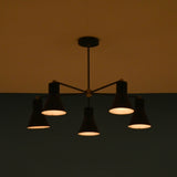 Atmospheric view of 5 cone brass chandelier casting warm industrial lighting in modern space