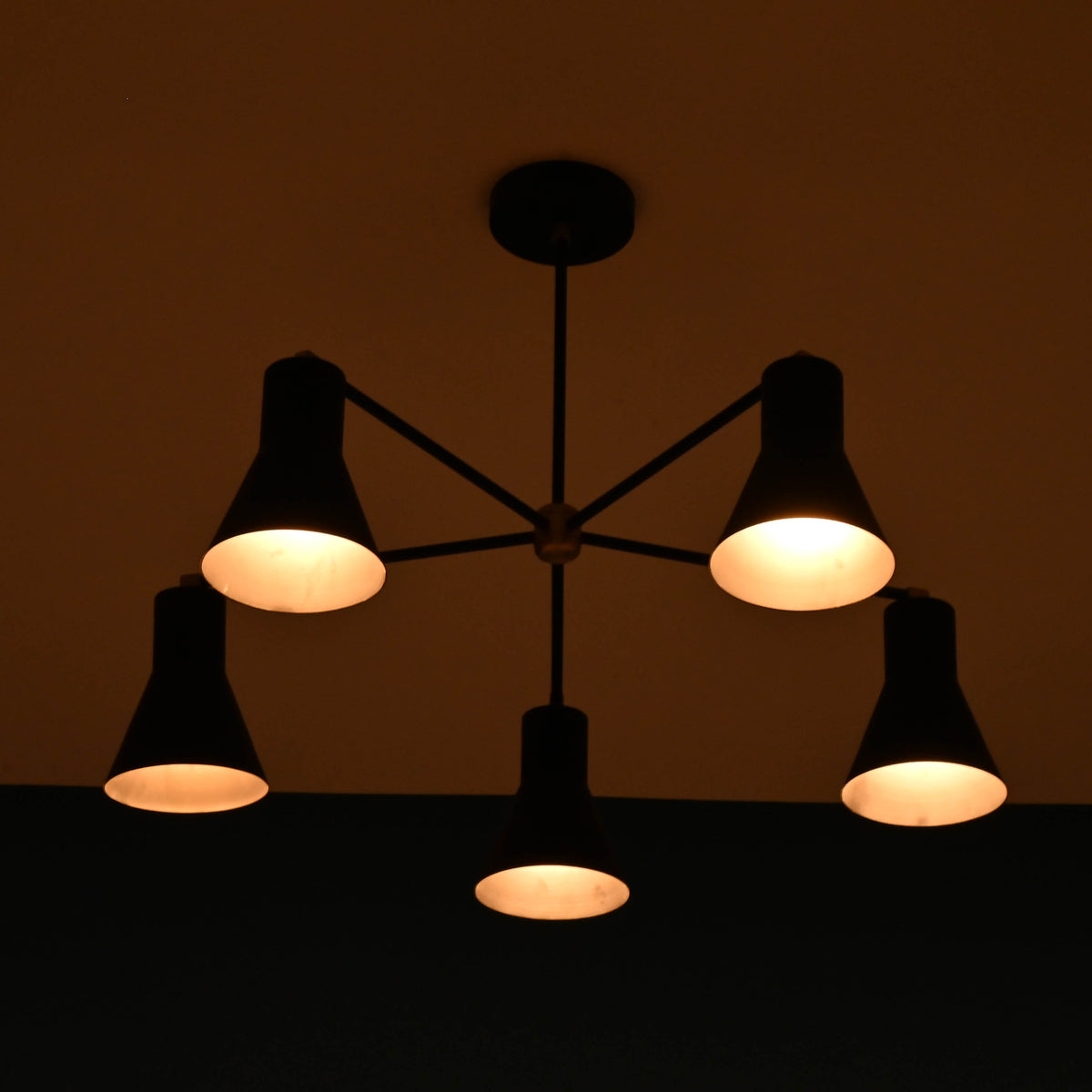 Modern brass 5 cone chandelier illuminated in dark room creating warm ambient lighting effect