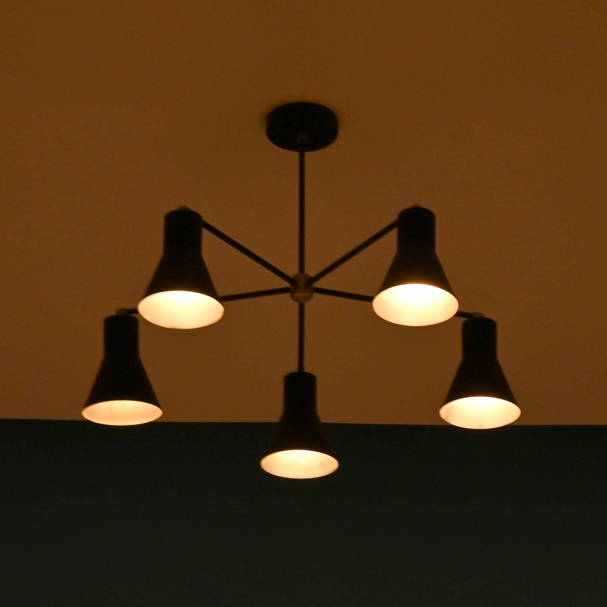 Soft ambient lighting from modern brass 5 cone chandelier in low light interior setting