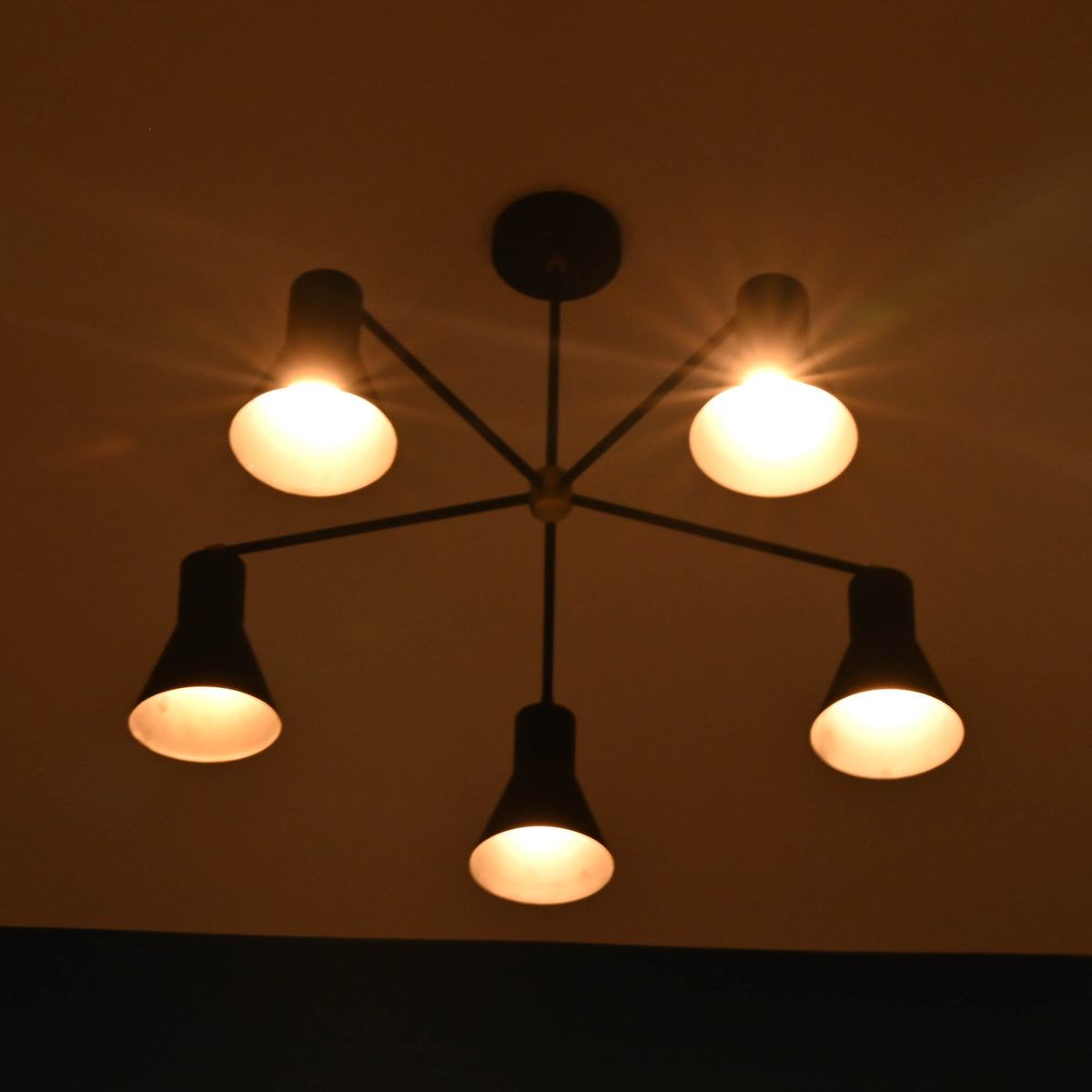 Close view of 5 cone brass chandelier showing warm light diffusion through metal cone shades