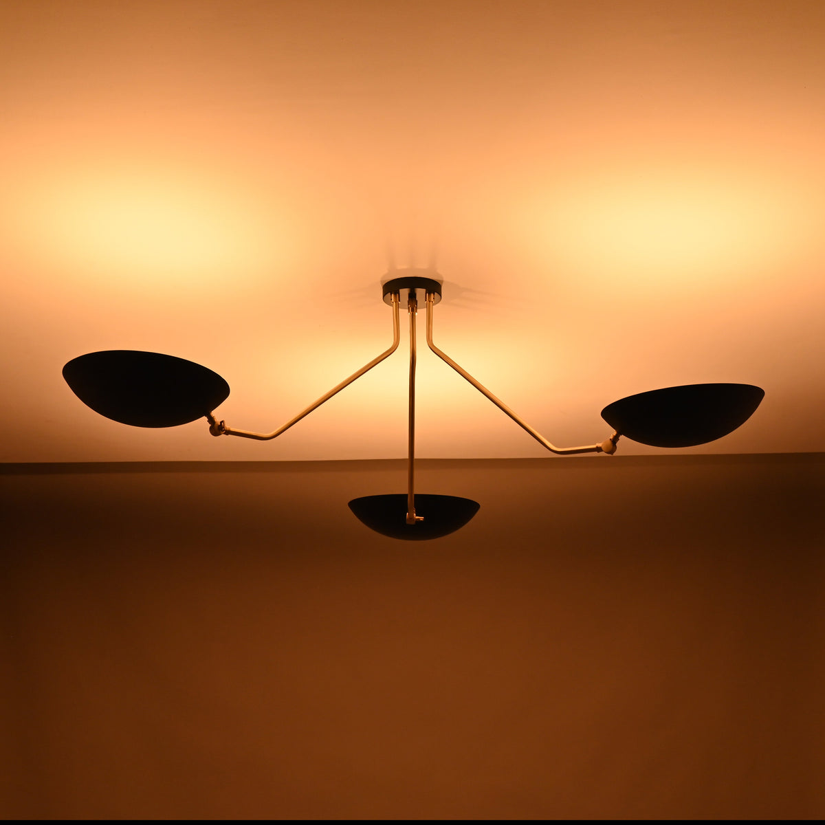 Modern brass-arm chandelier with three matte black bowl shades casting soft, warm ceiling illumination.