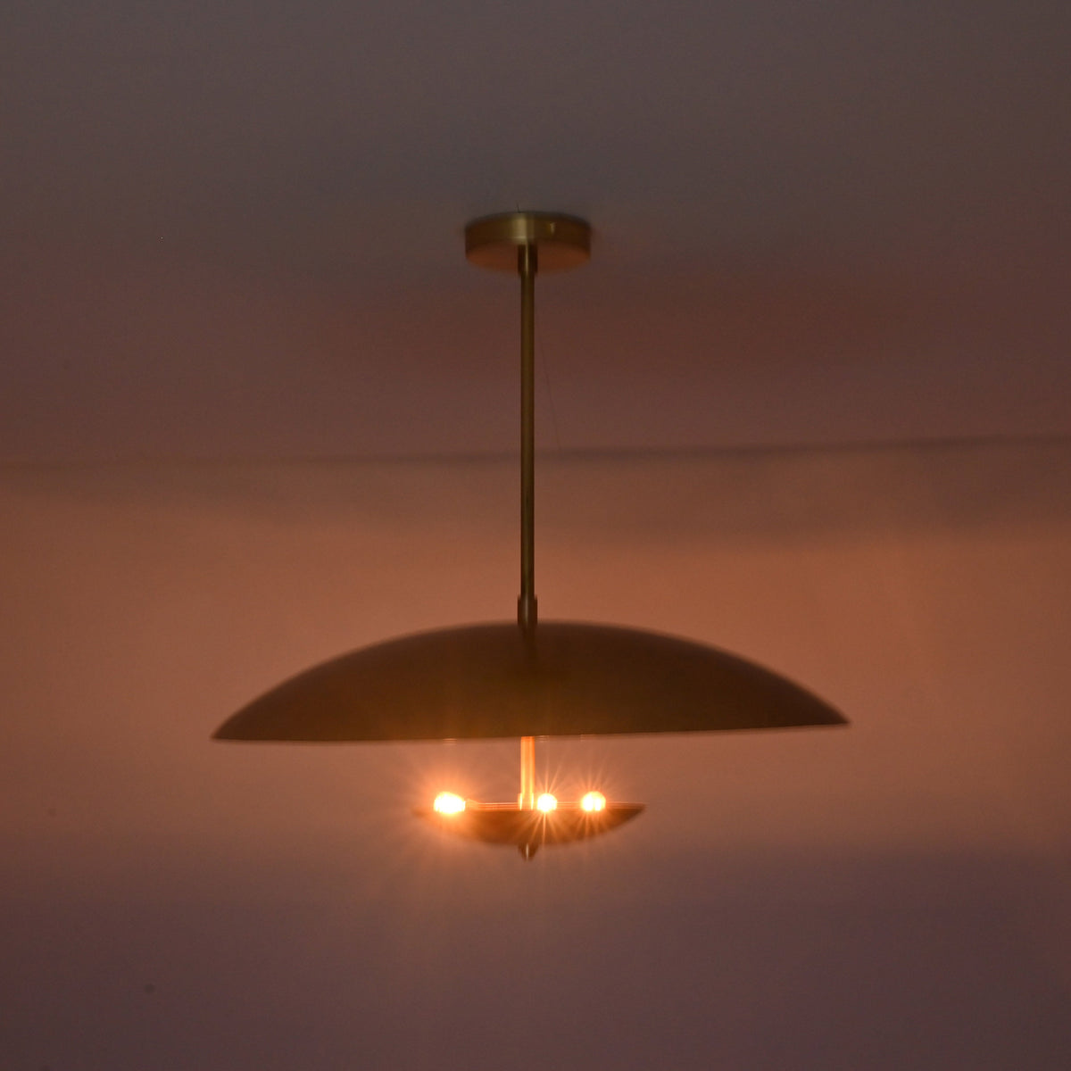 Modern brass bowl pendant glowing warmly with indirect light and minimalist ceiling design.