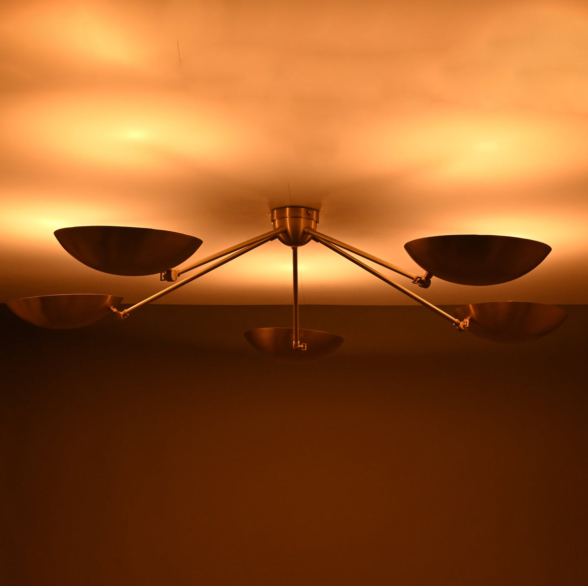 Modern brass ceiling light producing indirect upward glow through sculpted bowl-shaped shades.