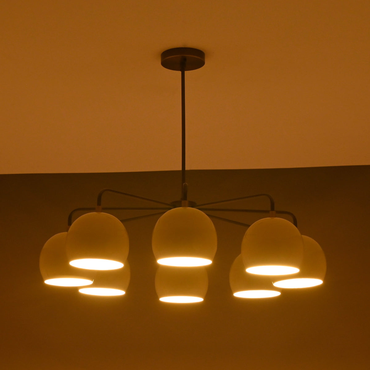 Minimalist 8-light chandelier in brass with soft evening light illuminating ivory dome shades.