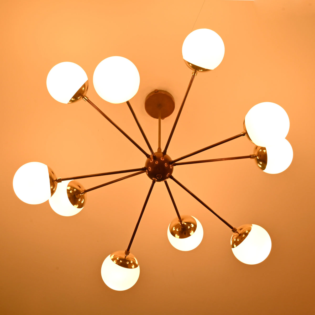 Low angle view of a modern brass chandelier with glowing glass globes highlighting sculptural radiating arms.