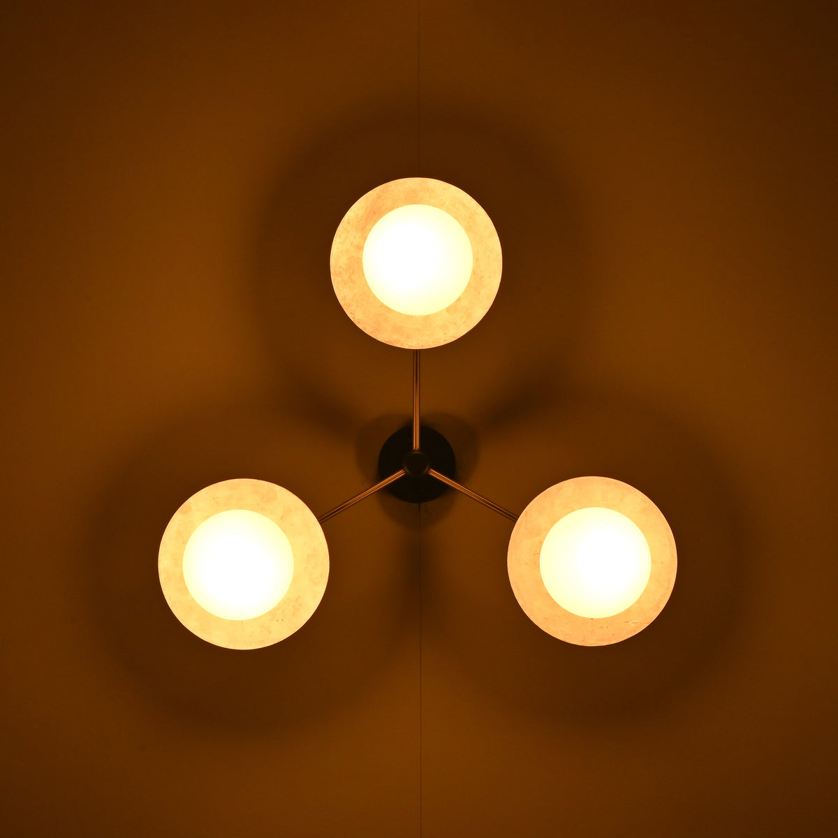 Brass disc flush mount ceiling light glowing warmly in a dark interior, highlighting opal glass globes.